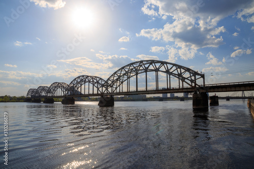 Vintage through (tied) arch railway steel bridge (Dzelzcela tilts) over Daugava river in Riga, Latvia on a sunny day with clouds in a blue sky. photo