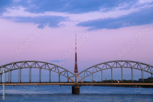 Vintage through (tied) arch railway bridge (Dzelzcela tilts) over Daugava river and the radio and TV tower (televizijas tornis) in Riga, Latvia at dawn, after sunset, with blue clouds in a pink sky. photo