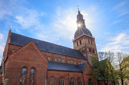 Cathedral on Dome Square (Doma Laukums) on a sunny day with clouds in a blue sky, in Riga, Latvia. Sun is directly behind the bell tower and light is passing through an opening in it, making a star. photo