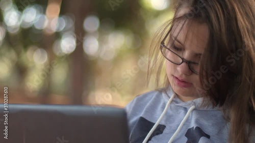 Beautiful teenager girl with glasses on a park bench with a laptop. Studying in the fresh air. Concentration. Think.