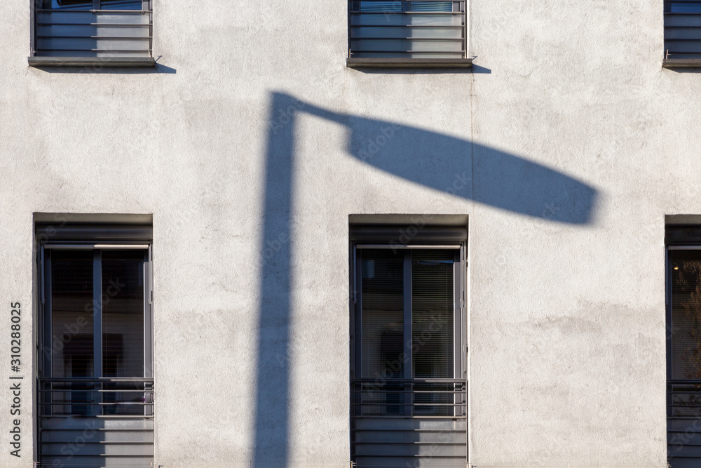 Shadow of a street light on the white facade of a modern building.