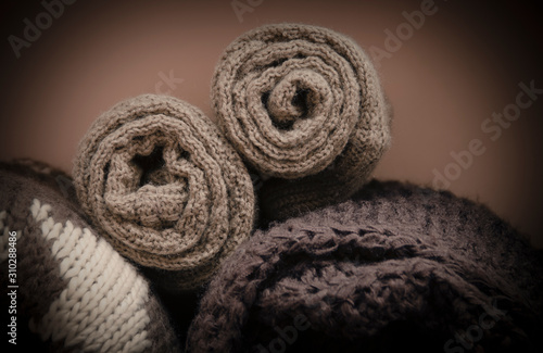 Knitted winter clothes twisted into tubes. Textile brown background.