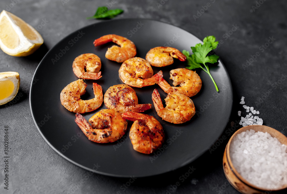 grilled shrimps, with lemons, herbs and spices, served on a black plate on a stone background grilled shrimps, with lemons, herbs and spices, served on a black plate on a stone background