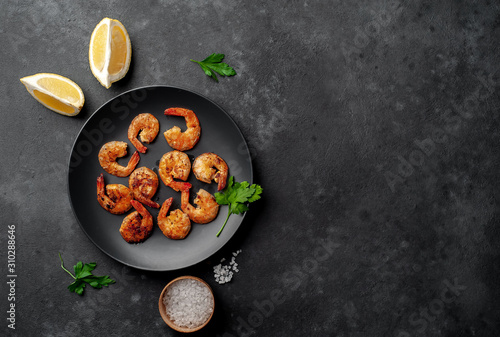 grilled shrimps, with lemons, herbs and spices, served on a black plate on a stone background with copy space for your text
