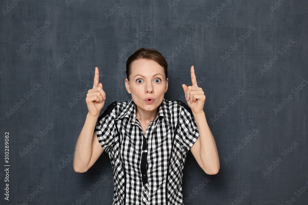 Portrait of surprised shocked girl pointing at copy space on top Portrait of surprised shocked girl pointing at copy space on top