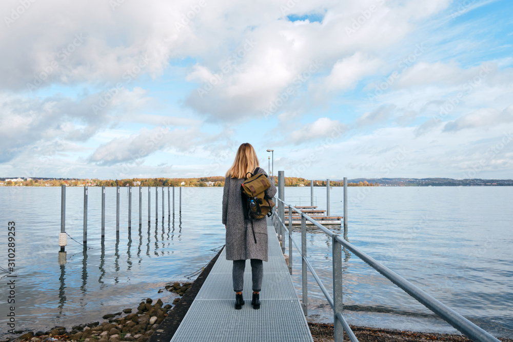 Beautiful caucasian woman stands on pier in Kreuzlingen. Girl in travel. Bodensee lake on the border with Germany. Landscape in Switzerland. Amazing scenic outdoors view. Adventure lifestyle