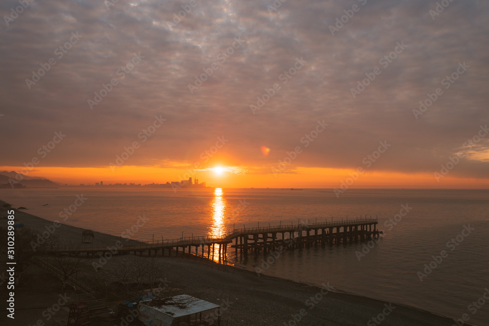 Beautiful sunset on the sea with bright sun and a pier in the city of Batumi. Georgia