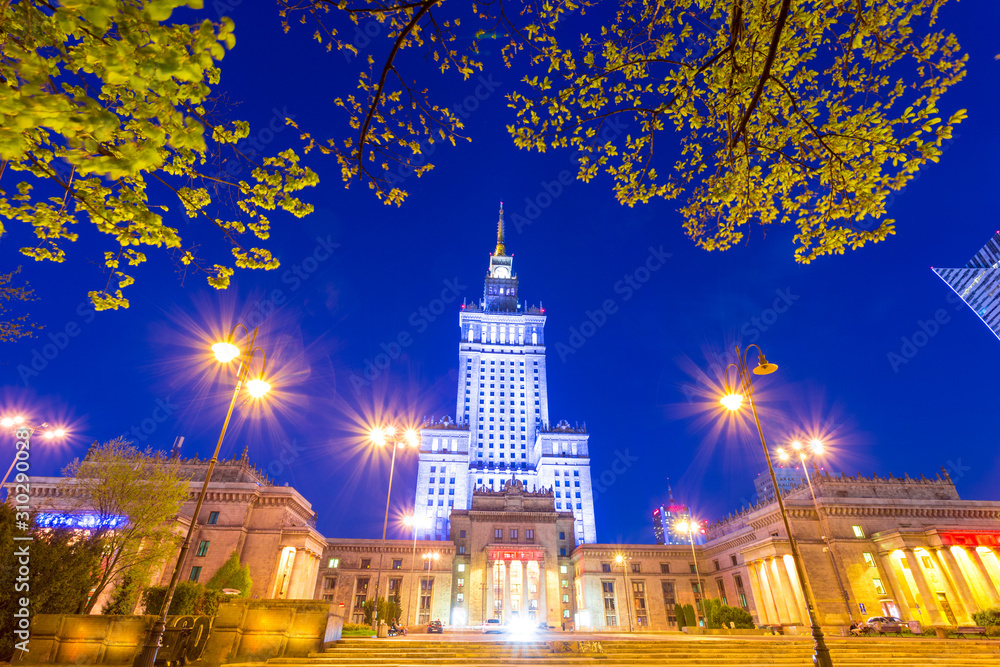 Palace of Culture and Science in downtown Warsaw, Poland at night. Historical art deco building from the Soviet era at dusk, under clear blue sky.