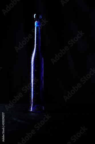 Elegant blue bottle of expensive wine gift with drops of water on a black background isolated