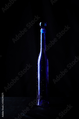 Elegant blue bottle of expensive wine gift with drops of water on a black background isolated