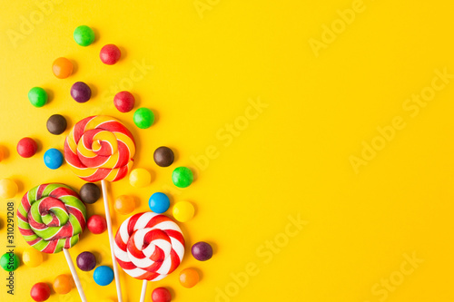 Three colorful round candies on sticks over yellow background with copy space. Closeup view