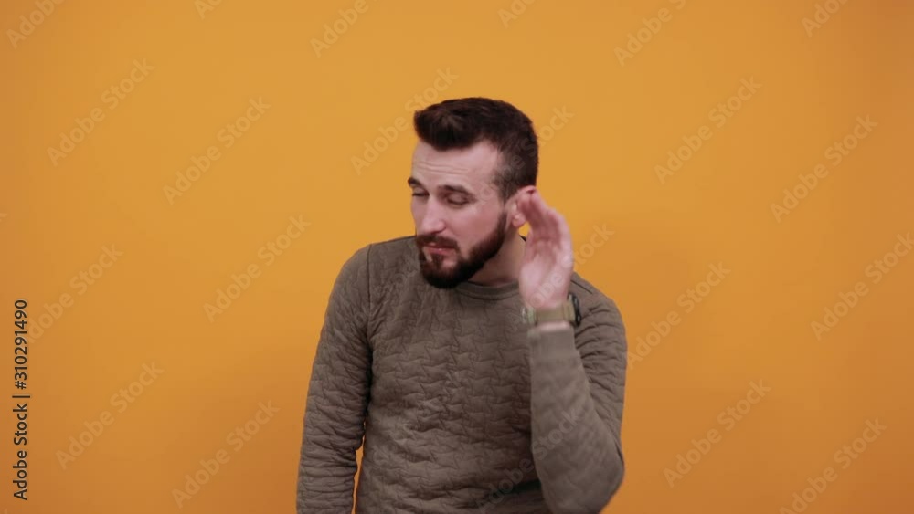 Young handsome caucasian man over isolated orange background looking at camera, keeping hand on ear, listening, gossip concept, wearing fashion green sweater Young handsome caucasian man over isolated orange background looking at camera, keeping hand on ear, listening, gossip concept, wearing fashion green sweater