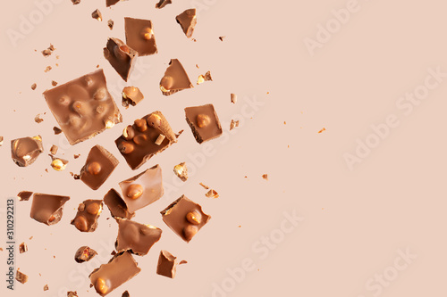 Flying in the air broken bar of milk chocolate with nuts and flakes on pastel pink background.  Chocolate pieces levitation concept.