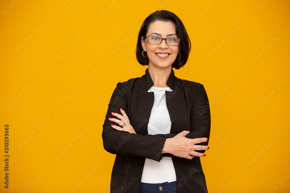 Attractive middle aged woman with beautiful smile on yellow wall. Pretty older business woman, successful confidence with arms crossed. Attractive middle aged woman with beautiful smile on yellow wall. Pretty older business woman, successful confidence with arms crossed.