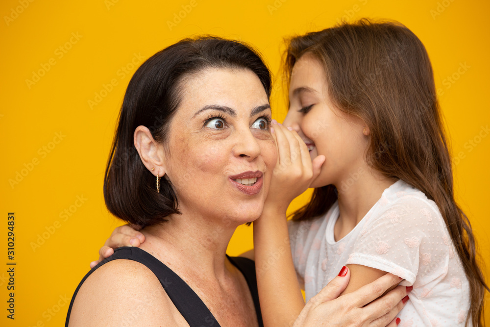 Mom and daughter secretive. kid sharing a secret with mother. Mommy little kid daughter isolated on yellow background studio portrait. Mother's Day love family parenthood childhood concept Mom and daughter secretive. kid sharing a secret with mother. Mommy little kid daughter isolated on yellow background studio portrait. Mother's Day love family parenthood childhood concept