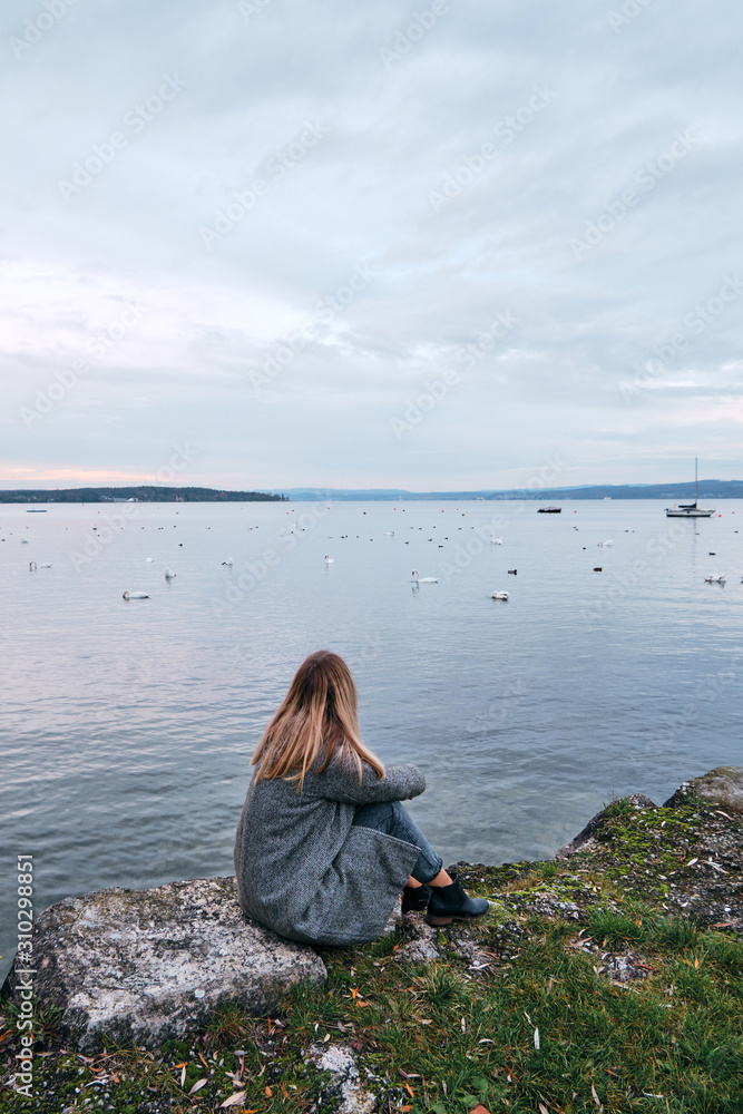 Beautiful blond hair woman enjoy panorama by the Bodensee lake. Landscape in Switzerland. Happy girl in travel. Amazing scenic outdoors view. Dramatic sky. Swans on water. Adventure lifestyle, freedom