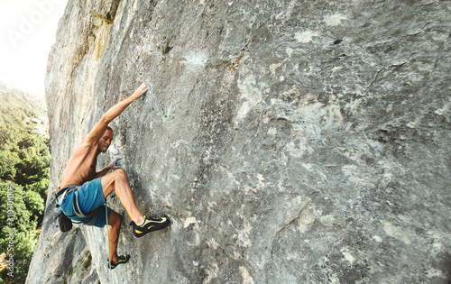 strong muscular man rock climber with naked torso dynamically climbing on a vertical cliff, making hard wide move and gripping hold.