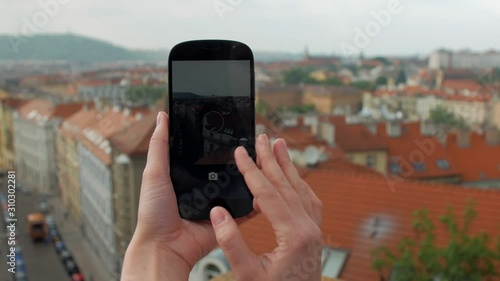 close-up view of female hands holding smartphone and taking photos of red roof buildings in Prague photo