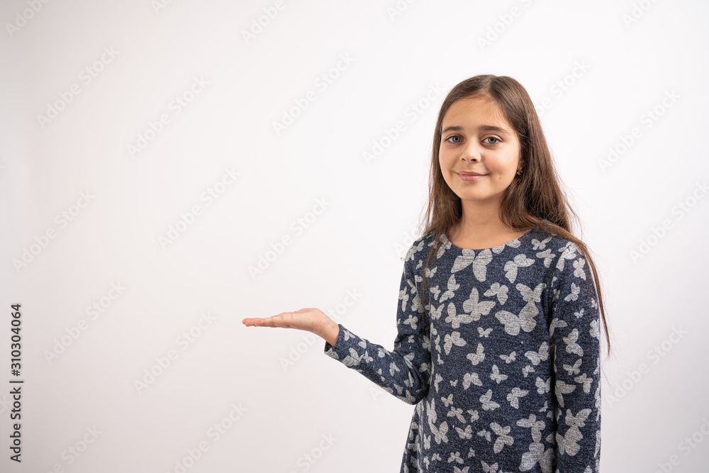 Waist up portrait of the attractive young brunette girl in blue dress that stands with raised opened palm, holds your product and looking at the camera, isolated over white background Waist up portrait of the attractive young brunette girl in blue dress that stands with raised opened palm, holds your product and looking at the camera, isolated over white background