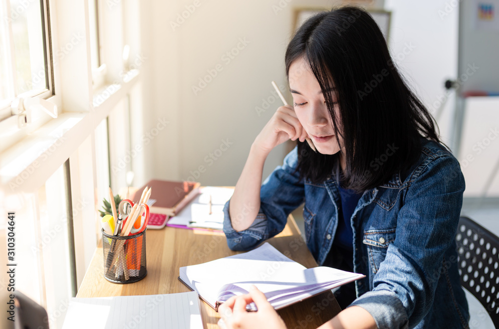 attractive asian female reading a book and lectures on notebook near glass windows, she rest chin on her hand and feeling relax, education time attractive asian female reading a book and lectures on notebook near glass windows, she rest chin on her hand and feeling relax, education time