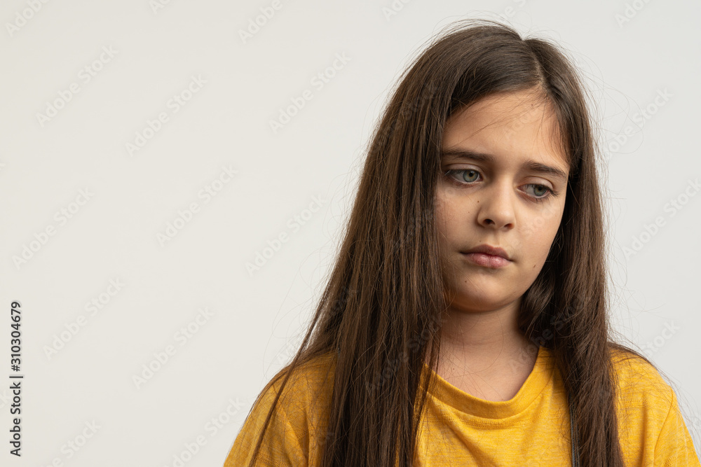 Waist up portrait of the upset, unhappy, sad brunette girl with loose hair, dressed in yellow t-shirt isolated over white background Waist up portrait of the upset, unhappy, sad brunette girl with loose hair, dressed in yellow t-shirt isolated over white background