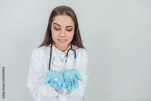 Lovely young doctor holding two small white pills in her palms  looking at them  thinking which of them to choose.