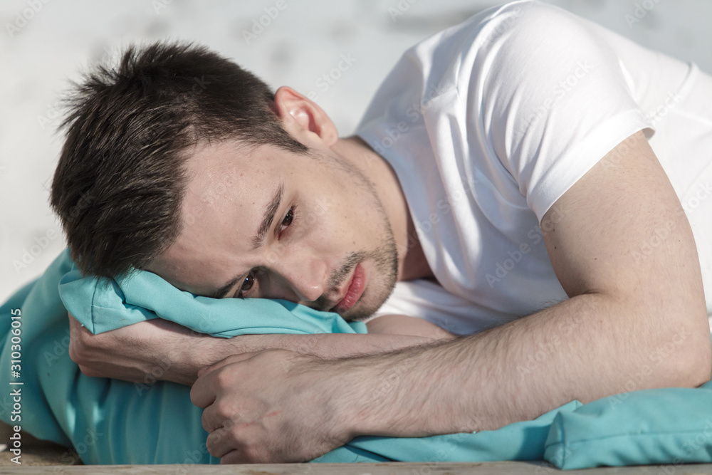 Fototapeta premium Young guy in white clothes depressed on a bed closeup
