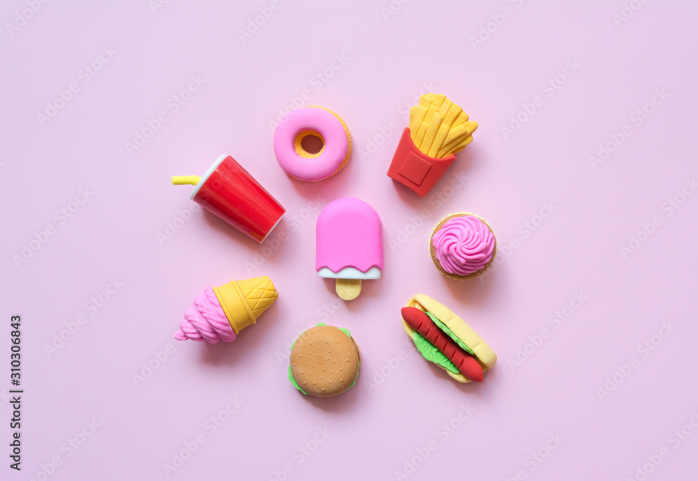 A variety of toy fast food and different sweets in miniature with shadows on a soft pink background.