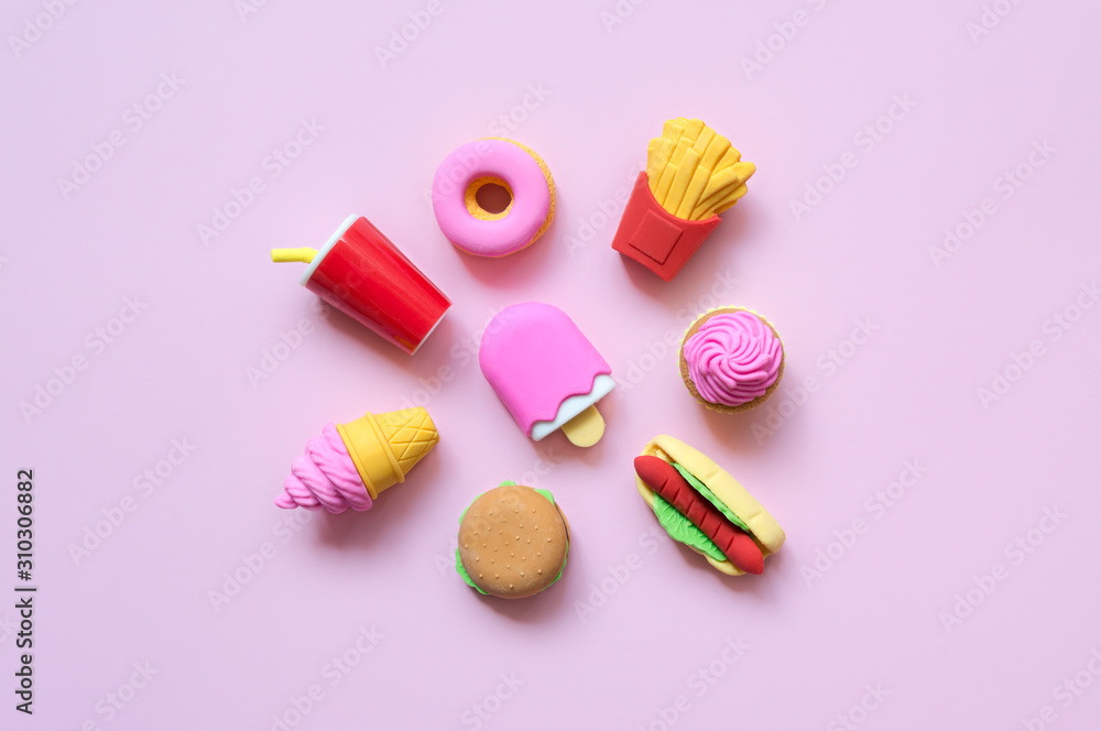 A variety of toy fast food and different sweets in miniature with shadows on a soft pink background. A variety of toy fast food and different sweets in miniature with shadows on a soft pink background.