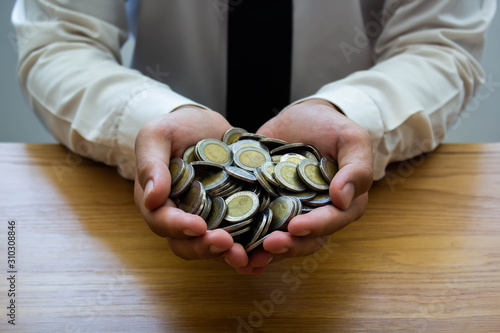 Business people use two hands to hold a lot of coins on wooden table.