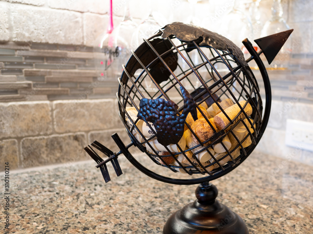 A metal globe containing used corks incribed with dates and notes from wine bottles on a granite kitchen countertop A metal globe containing used corks incribed with dates and notes from wine bottles on a granite kitchen countertop