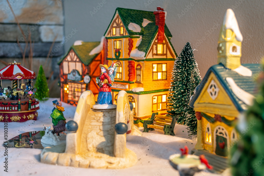A colorful, illuminated Christmas village decorated table with victorian buildings and miniature figurines