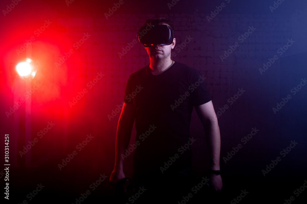 man in modern glasses of virtual reality holds wireless joysticks on a 3D background, a guy is a gamer with gaming gadgets