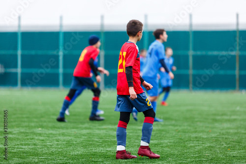 Boys in red and blue sportswear plays football on field, dribbles ball. Young soccer players with ball on green grass. Training, football, active lifestyle for kids concept