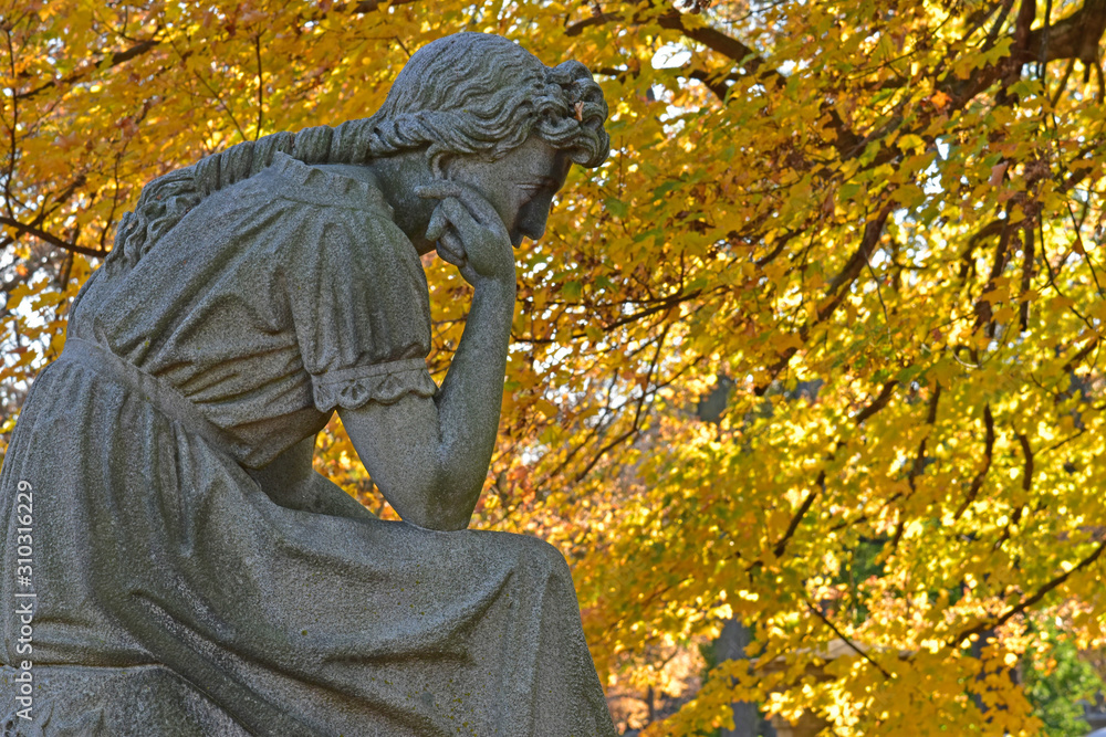 Fall foliage backs a pondering statue in a cemetery