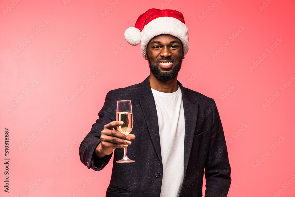 Young african man in santa hat drinking champagne isolated on red background Young african man in santa hat drinking champagne isolated on red background