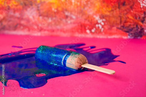 Sausage on sticks in blue sparkle paint. On a pink and orange textured background, top view photo.