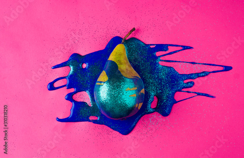 Ripe yellow pear in blue sparkle paint. On a pink background, photo from above.