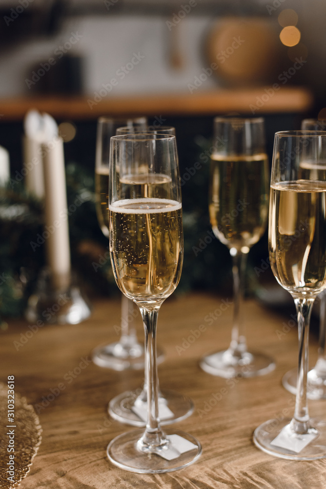 Group of glasses of luxury champagne on a wooden table. White wine in glasses of champagne against the background of a Christmas tree and garland lights Group of glasses of luxury champagne on a wooden table. White wine in glasses of champagne against the background of a Christmas tree and garland lights