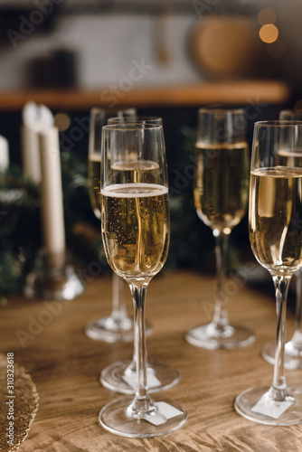 Group of glasses of luxury champagne on a wooden table. White wine in glasses of champagne against the background of a Christmas tree and garland lights