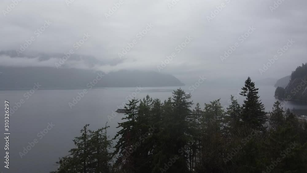 Mountains covered with the fog and clouds, behind the river. And pine trees in front. Mountains covered with the fog and clouds, behind the river. And pine trees in front.