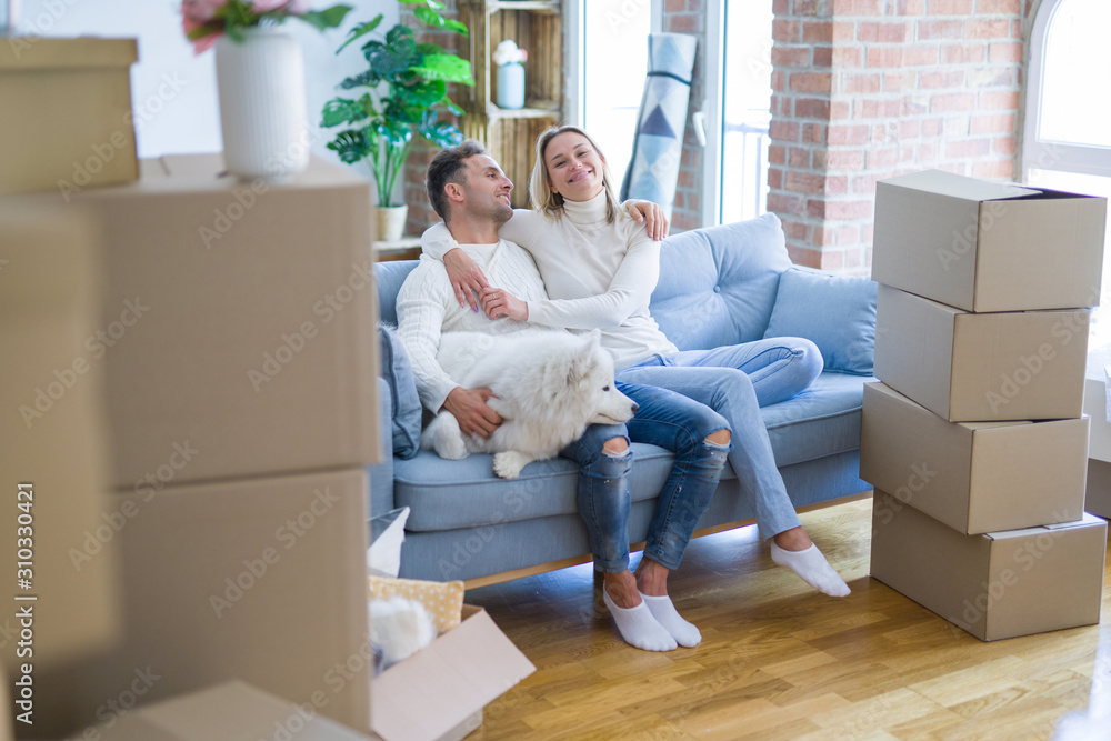 Young beautiful couple with dog kissing sitting on the sofa at new home around cardboard boxes Young beautiful couple with dog kissing sitting on the sofa at new home around cardboard boxes