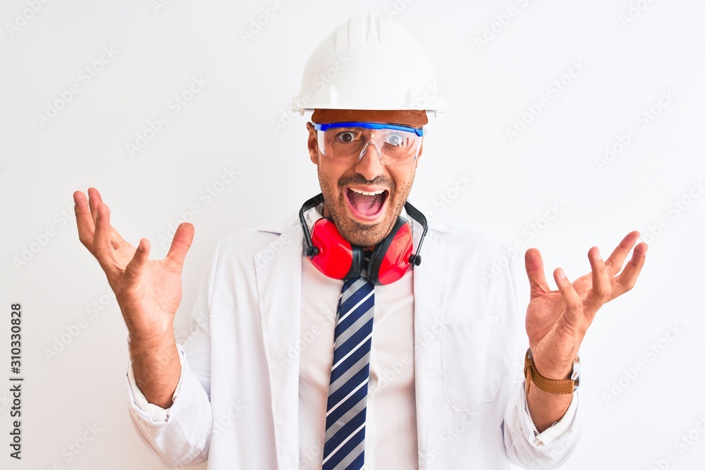 Young chemist man wearing security helmet and headphones over isolated background celebrating crazy and amazed for success with arms raised and open eyes screaming excited. Winner concept Young chemist man wearing security helmet and headphones over isolated background celebrating crazy and amazed for success with arms raised and open eyes screaming excited. Winner concept
