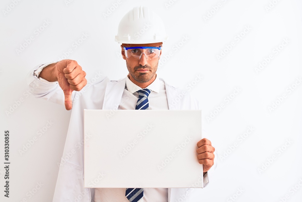 Young chemist man wearing security helmet holding signboard over isolated background with angry face, negative sign showing dislike with thumbs down, rejection concept Young chemist man wearing security helmet holding signboard over isolated background with angry face, negative sign showing dislike with thumbs down, rejection concept