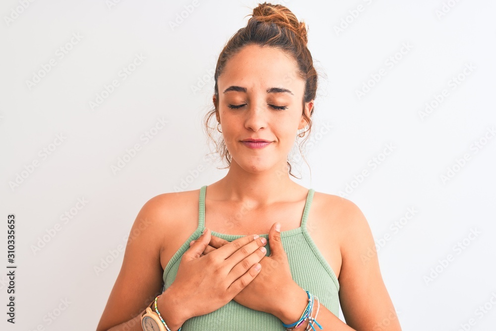 Young redhead woman wearing a bun over isolated background smiling with hands on chest with closed eyes and grateful gesture on face. Health concept.