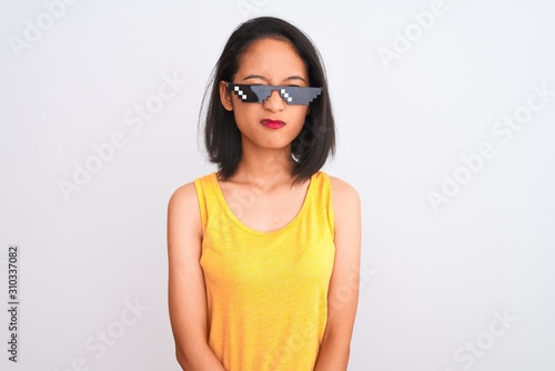 Young beautiful chinese woman wearing thug life sunglasses over isolated white background with serious expression on face. Simple and natural looking at the camera.