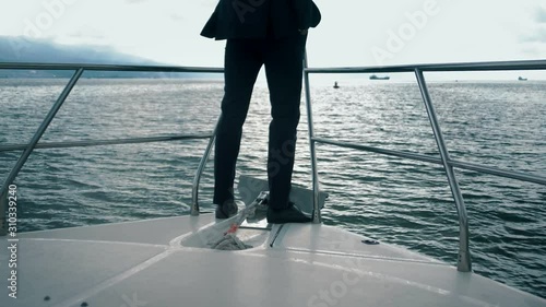 Rich successful man in a tuxedo stands on the nose of his huge yacht, sails across the ocean and looks into the distance. photo