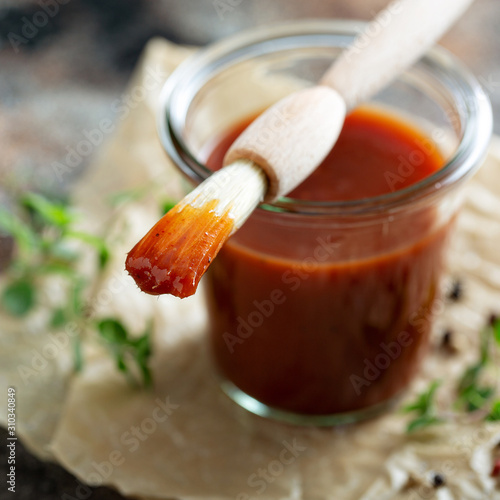 Foto Homemade sweet and spicy barbeque sauce with a basting brush in a jar