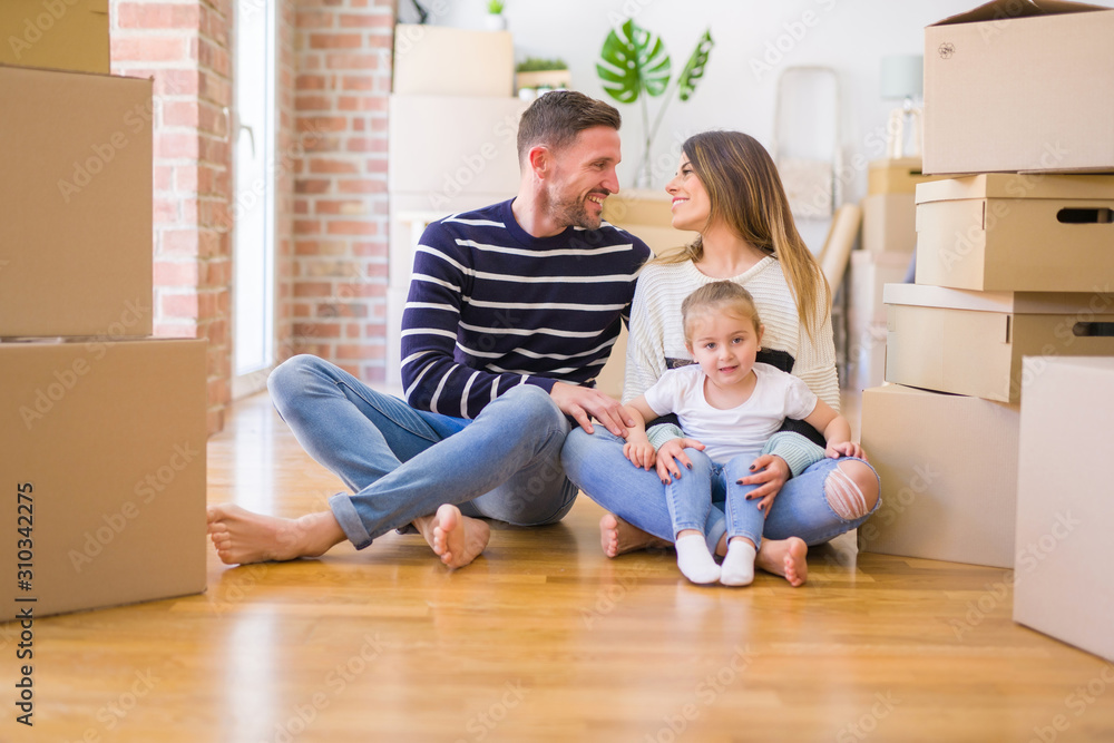 Beautiful family sitting on the floor playing with his kid at new home around cardboard boxes