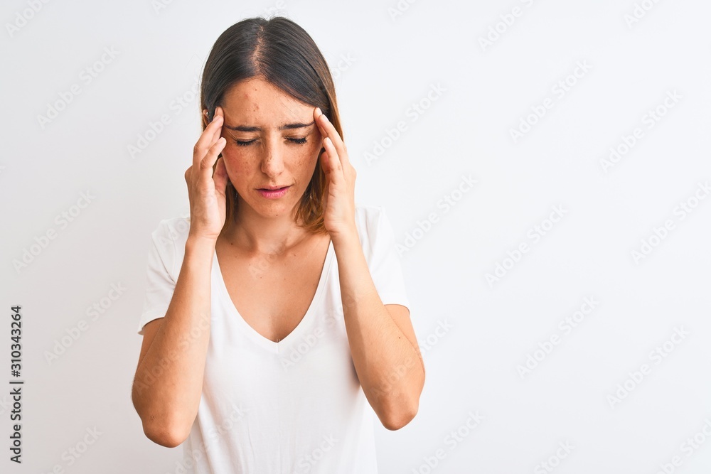 Beautiful redhead woman wearing casual white t-shirt over isolated background with hand on head for pain in head because stress. Suffering migraine. Beautiful redhead woman wearing casual white t-shirt over isolated background with hand on head for pain in head because stress. Suffering migraine.